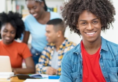 Studenten achter computer en 1 student kijkt lachend de camera in